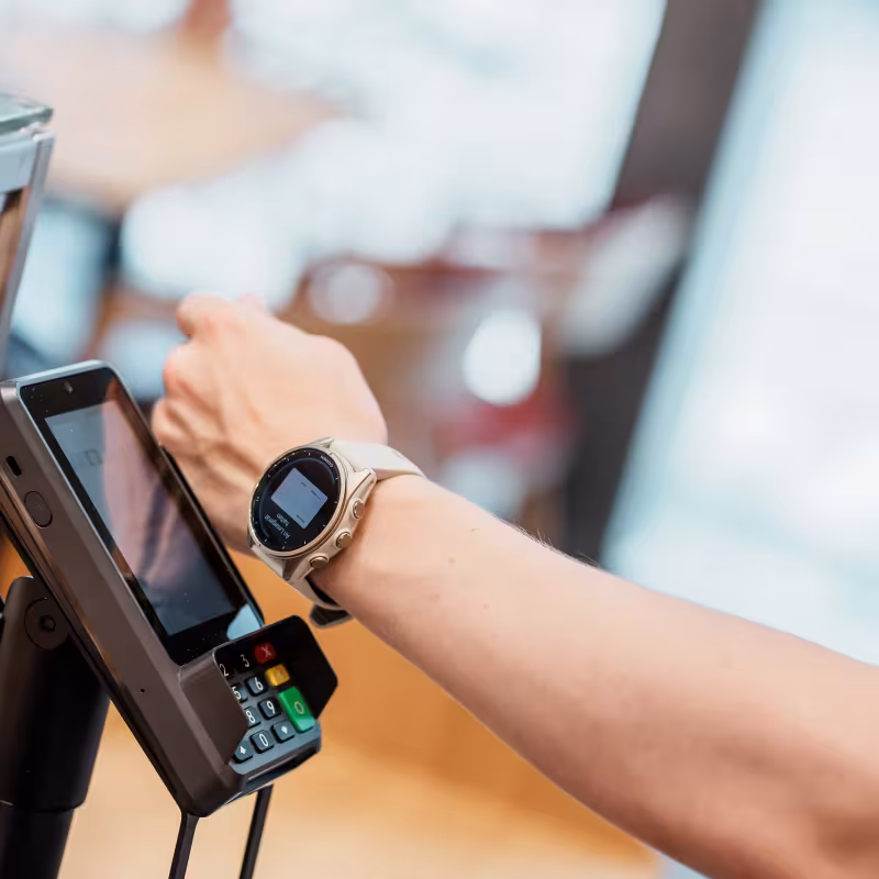 Arm mit Smartwatch hält Karte an Kartenterminal im Café