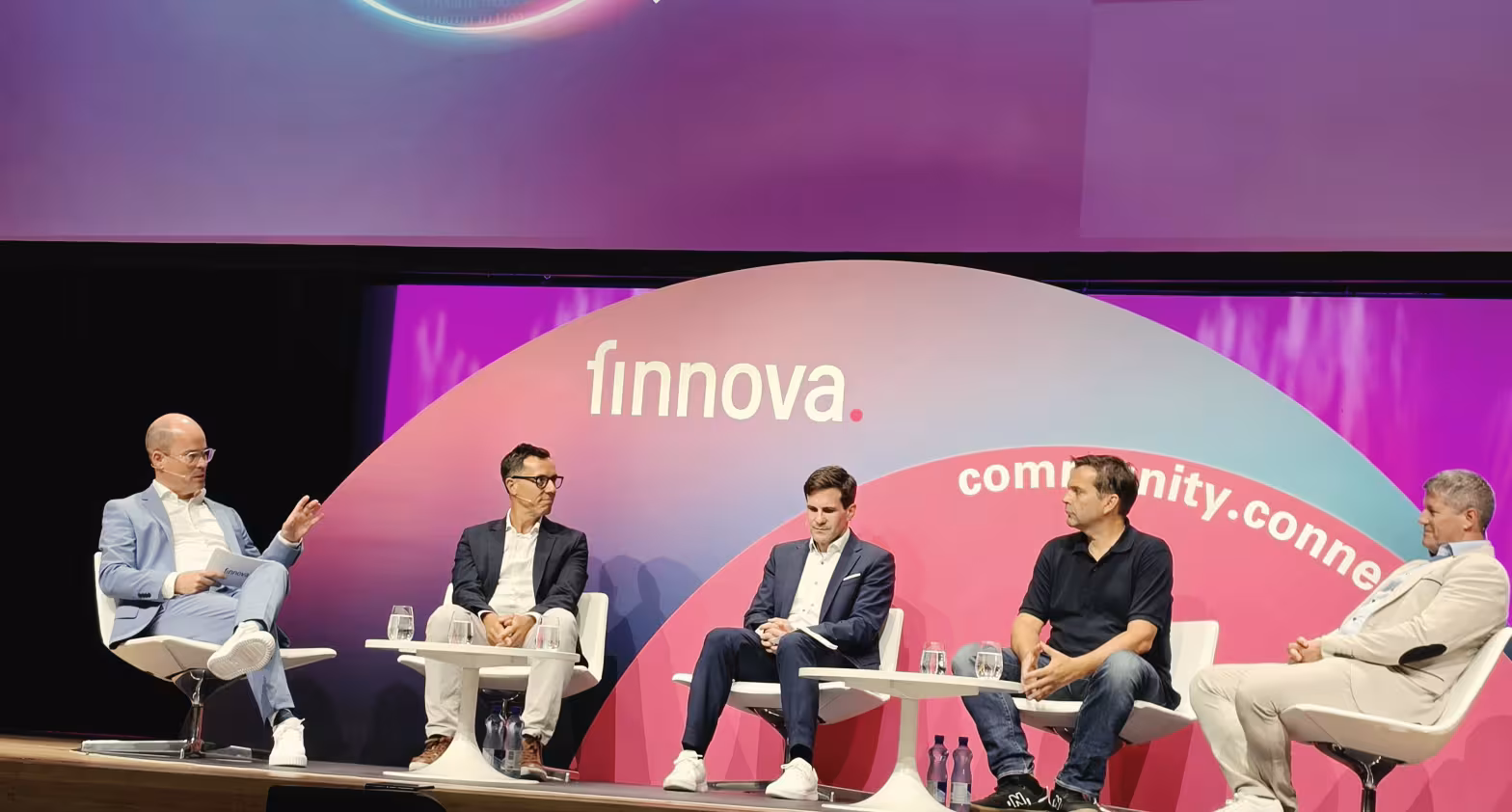 Podiumsdiskussion mit fünf Männern auf Bühne vor „finnovate“-Hintergrund in Rot‑Violett