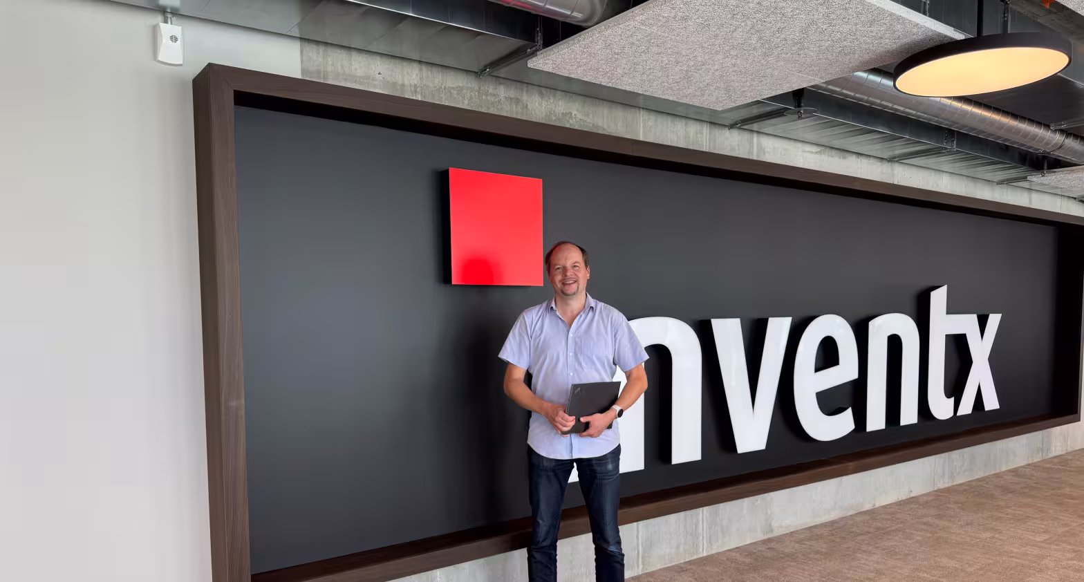 Mann steht im Büro vor großer Wand mit Inventx-Logo.