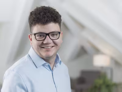 Porträtfoto eines lächelnden Mannes mit Brille im hellen Innenraum