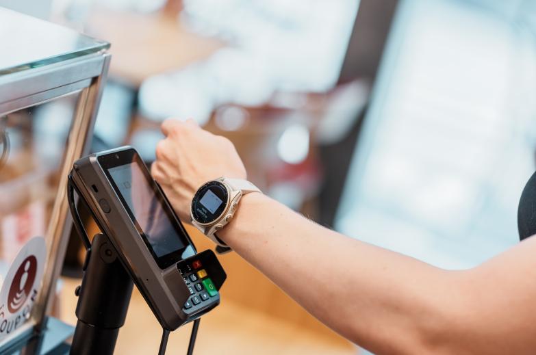 Arm mit Smartwatch hält Karte an Kartenterminal im Café