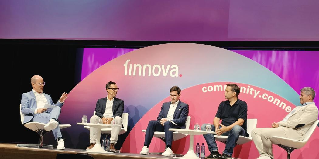 Podiumsdiskussion mit fünf Männern auf Bühne vor „finnovate“-Hintergrund in Rot‑Violett