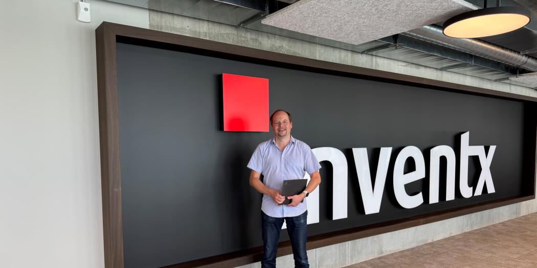 Mann steht im Büro vor großer Wand mit Inventx-Logo.
