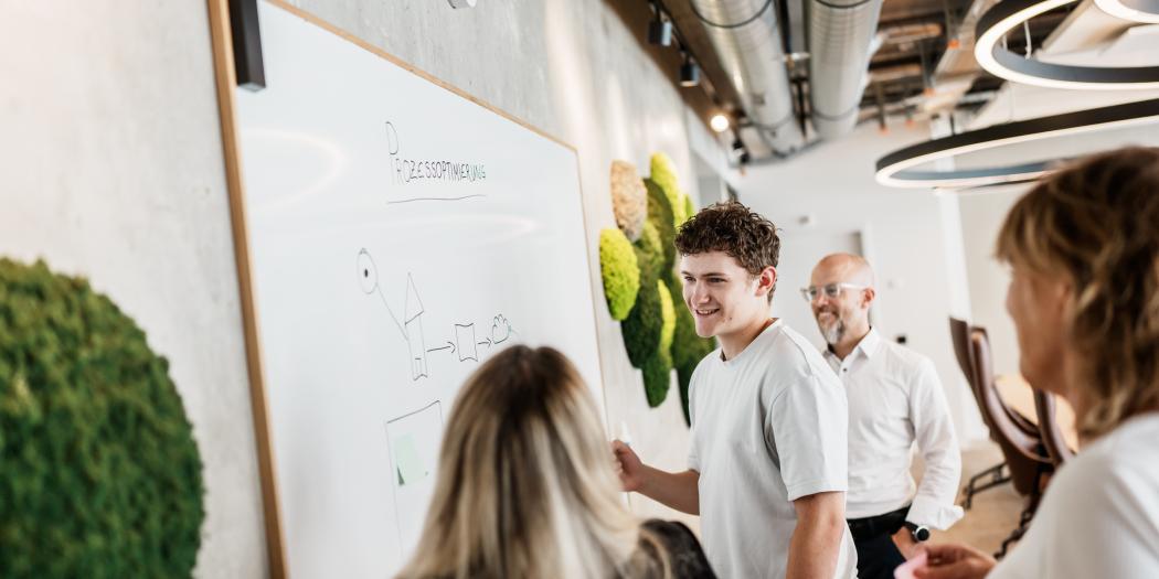 Teammeeting im Büro: Mann am Whiteboard, Kolleginnen melden sich.